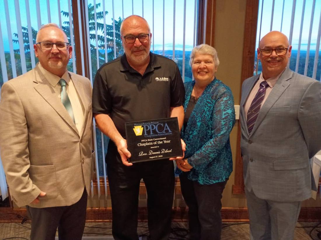 Dennis Dibert holding the County Chaplain of the Year plaque, standing with his wife Kathy and two colleagues